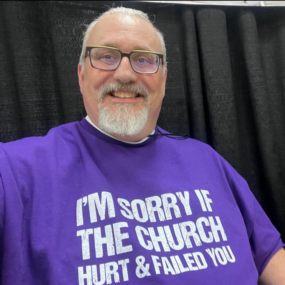 Derek White, wearing a shirt which reads, “I’m sorry if the church has hurt & failed you.”