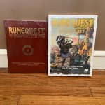 The Smoking Ruin book in a fantastic leatherette cover, and the Runequest Starter Set leaning up against a wall.