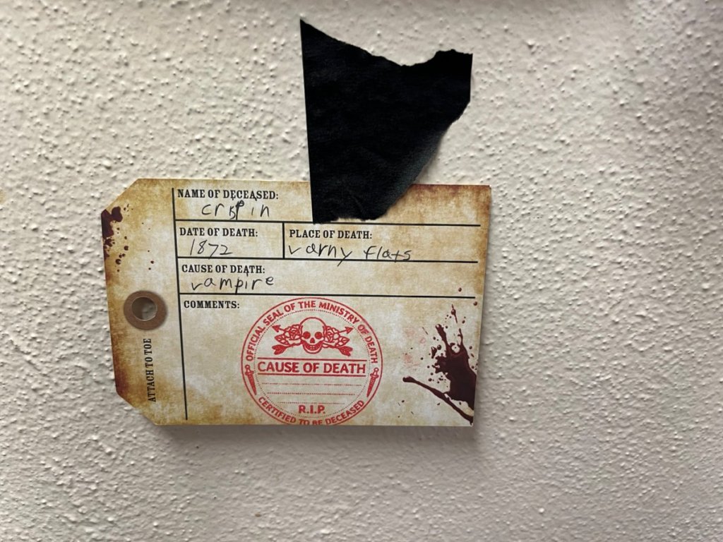 A toe-tag hangs on the wall of the fallen. Cause of Death was a vampire in 1872.