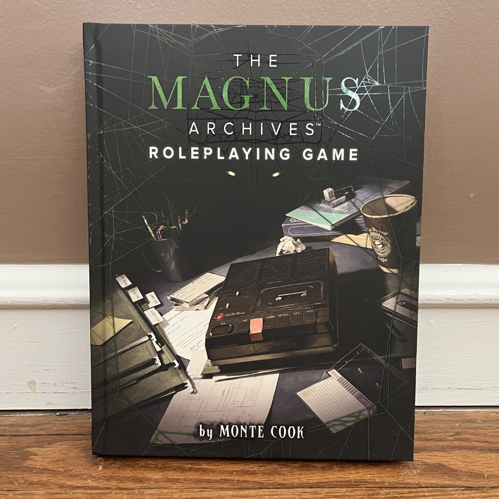 Magnus Archives rulebook, dark and brooding with books, papers, and an old-style cassette recorder.