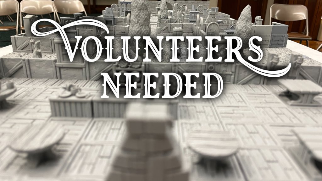 A miniature medieval city-scape retreats in the background. The words "Volunteers Needed" is overlayed in front.