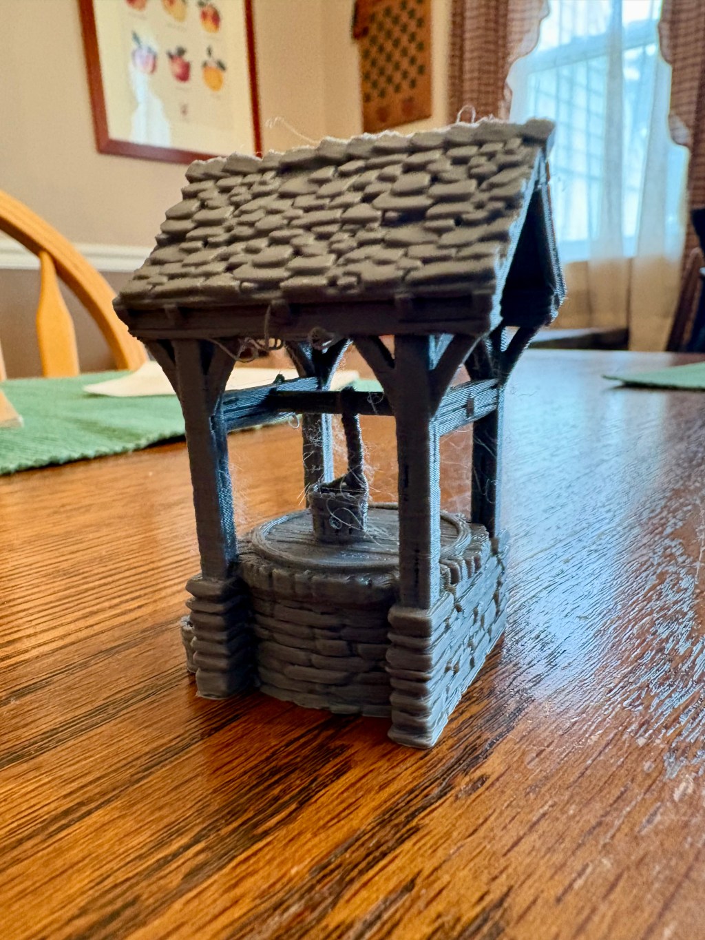 A 3d printed well, with a stone base and a slate roof. A bucket is placed on the well’s cover.