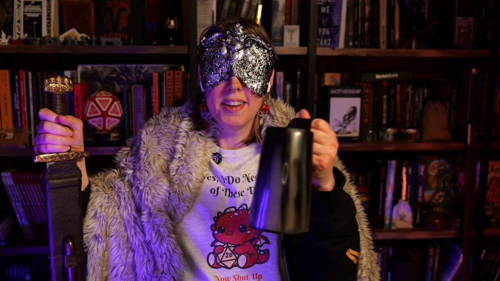Jen Cash in her blind bard glory, holding the sword in her right hand and a tankard of...something...in her left. She's wearing her signature silver mask.